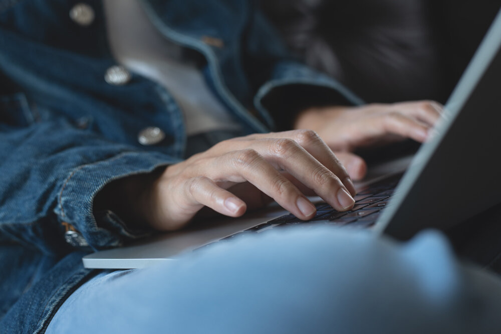A woman types on a laptop held on her lap.