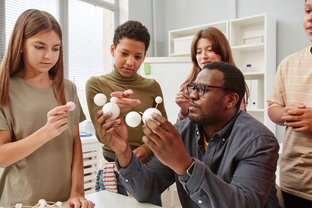 A teacher demonstrates a lesson with several children standing around him.