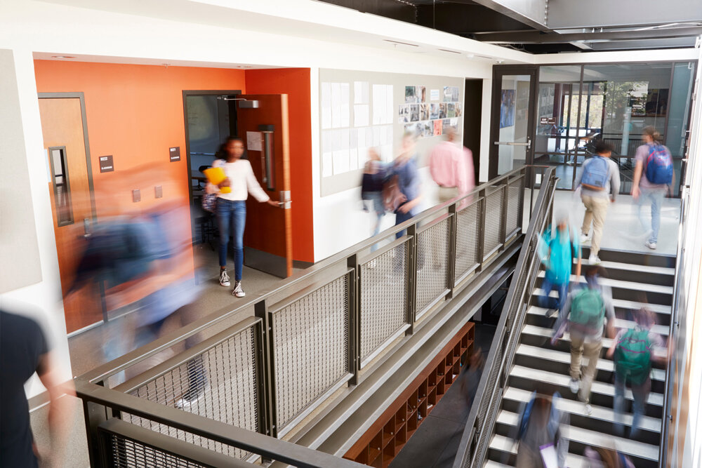 A blurred photo shows students walking between classes and up and down a stairwell.